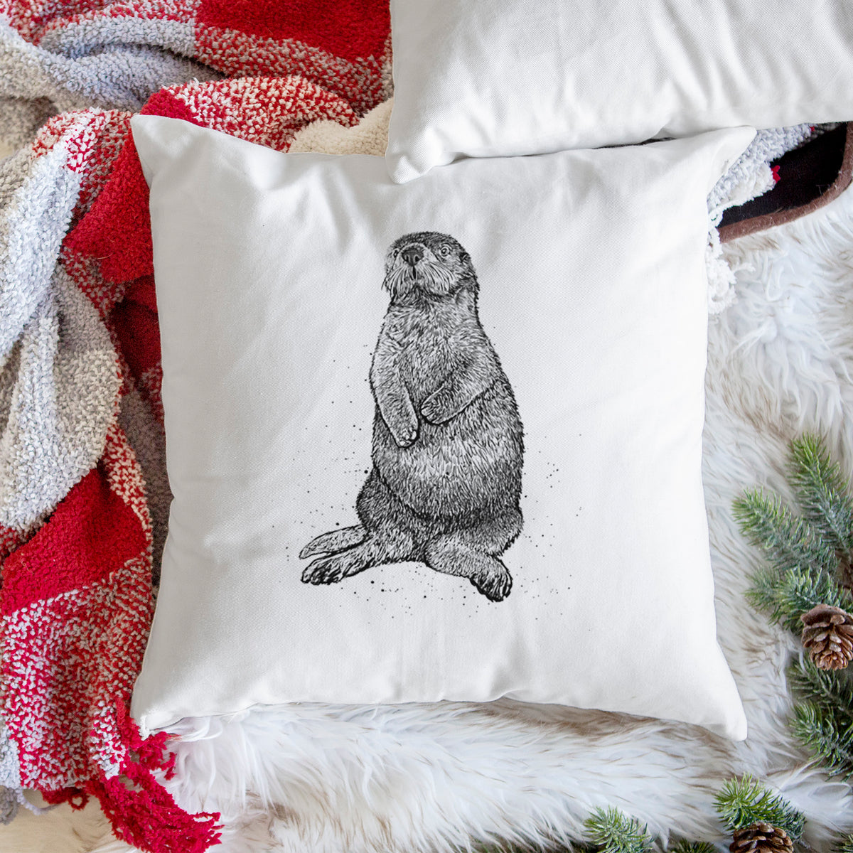 White pillow cover printed with a detailed black ink illustration of a sea otter sitting upright, on a woven chair.