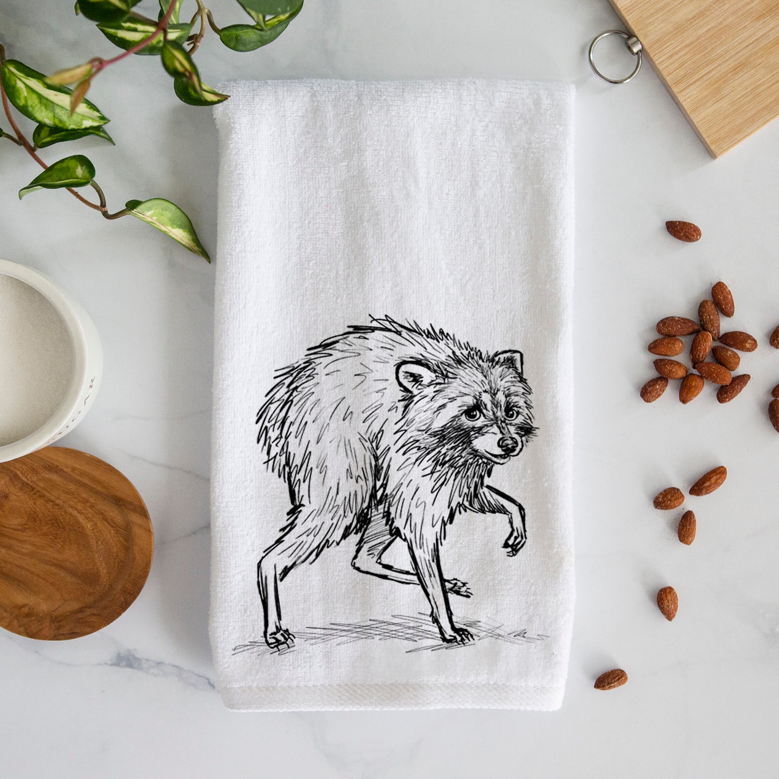 White hand towel printed with a detailed black ink illustration of a scruffy raccoon walking.