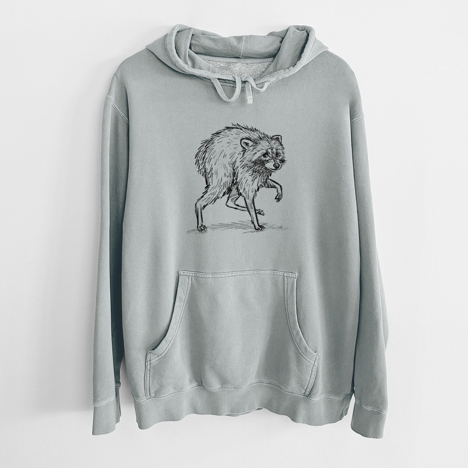 Sage green pigment dyed hoodie laid flat, printed with a detailed black ink illustration of a scruffy raccoon walking.