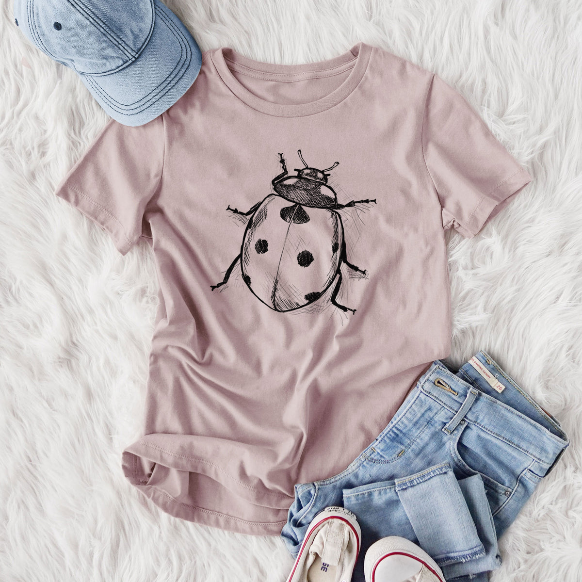 Women's relaxed fit cotton t-shirt printed with a detailed black ink illustration of a seven-spot ladybird beetle, styled flat on a white faux fur rug with jeans.