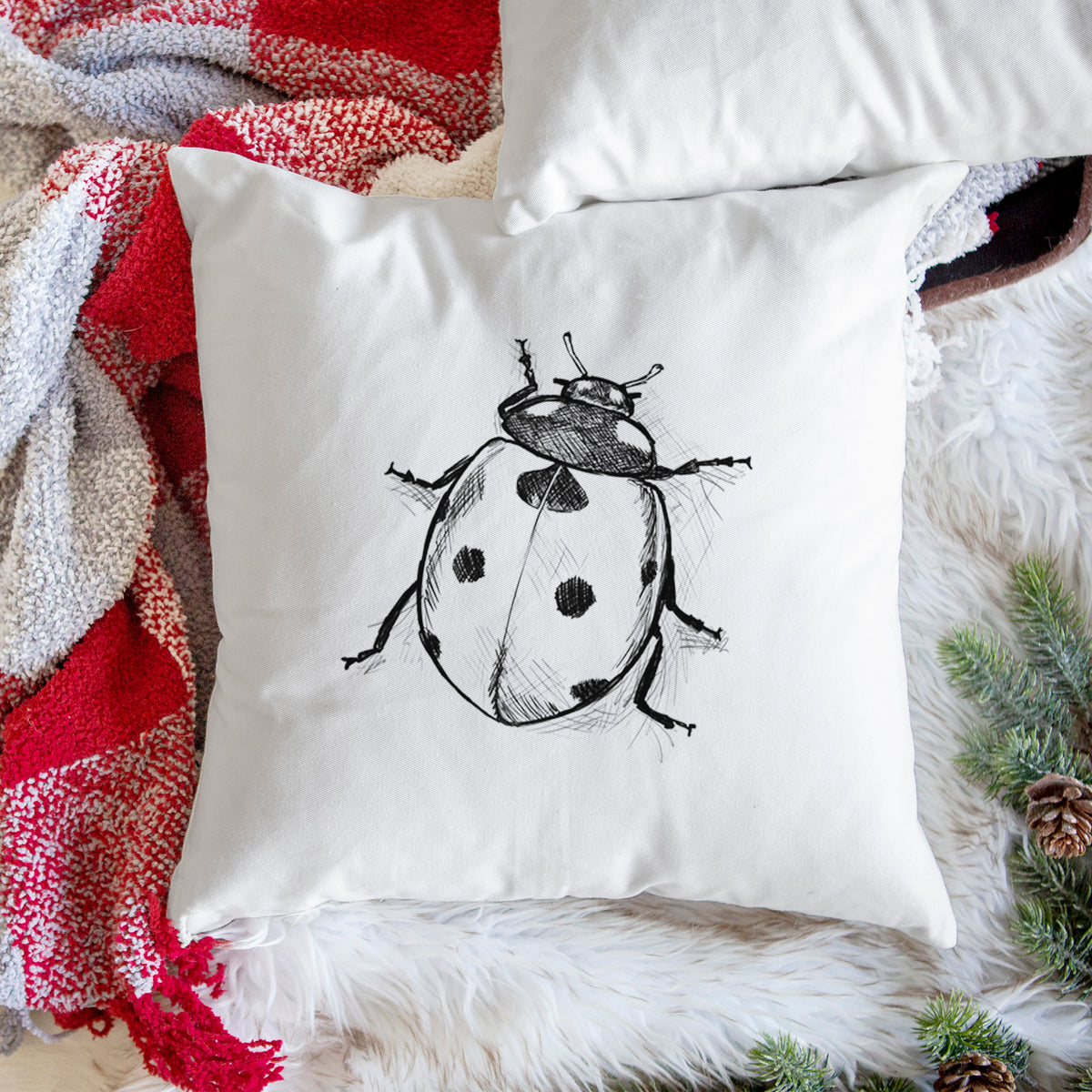 White pillow cover printed with a detailed black ink illustration of a seven-spot ladybird beetle, on a woven chair.