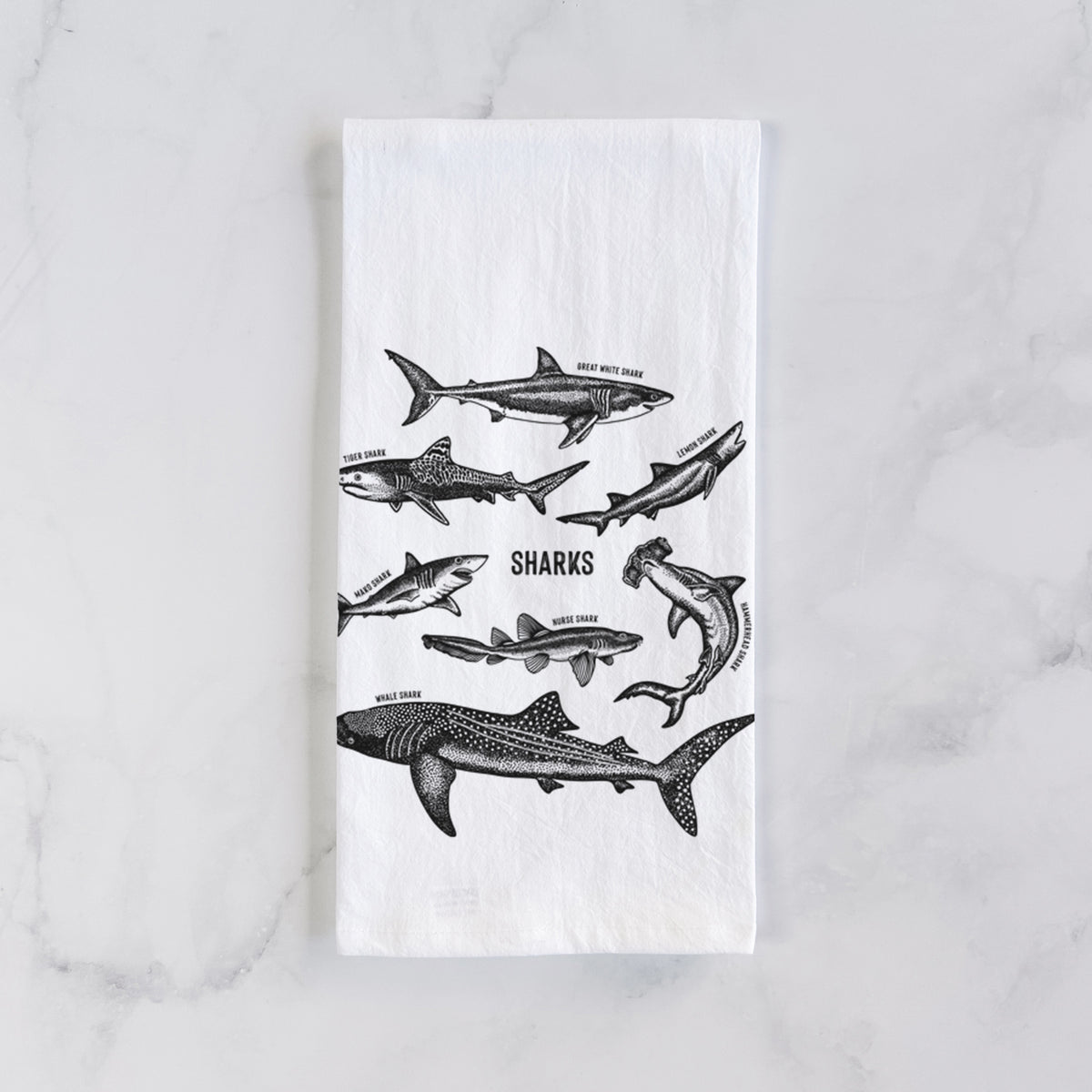 White cotton tea towel laid flat on marble, printed with a chart of black ink shark illustrations, including a whale shark, hammerhead and great white.