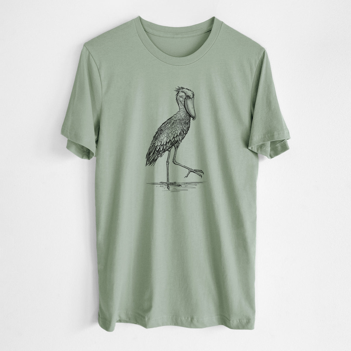 Sage green lightweight cotton t-shirt laid flat, printed with a black ink illustration of a shoebill stork standing on one leg.