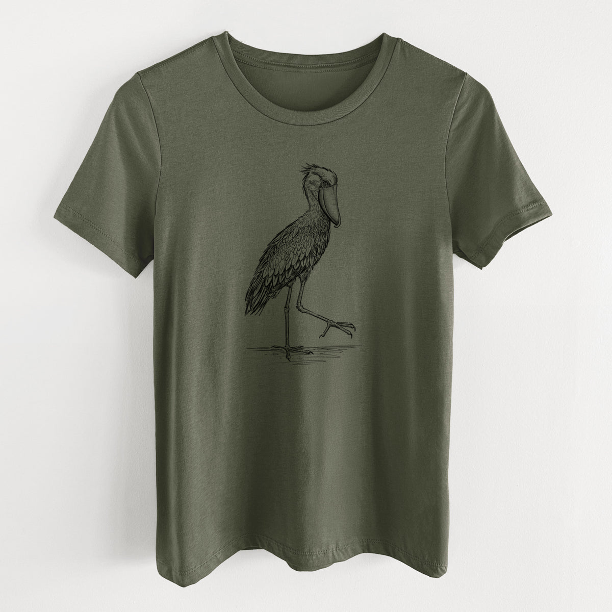 Military green women's relaxed fit cotton t-shirt laid flat, printed with a black ink illustration of a shoebill stork standing on one leg.