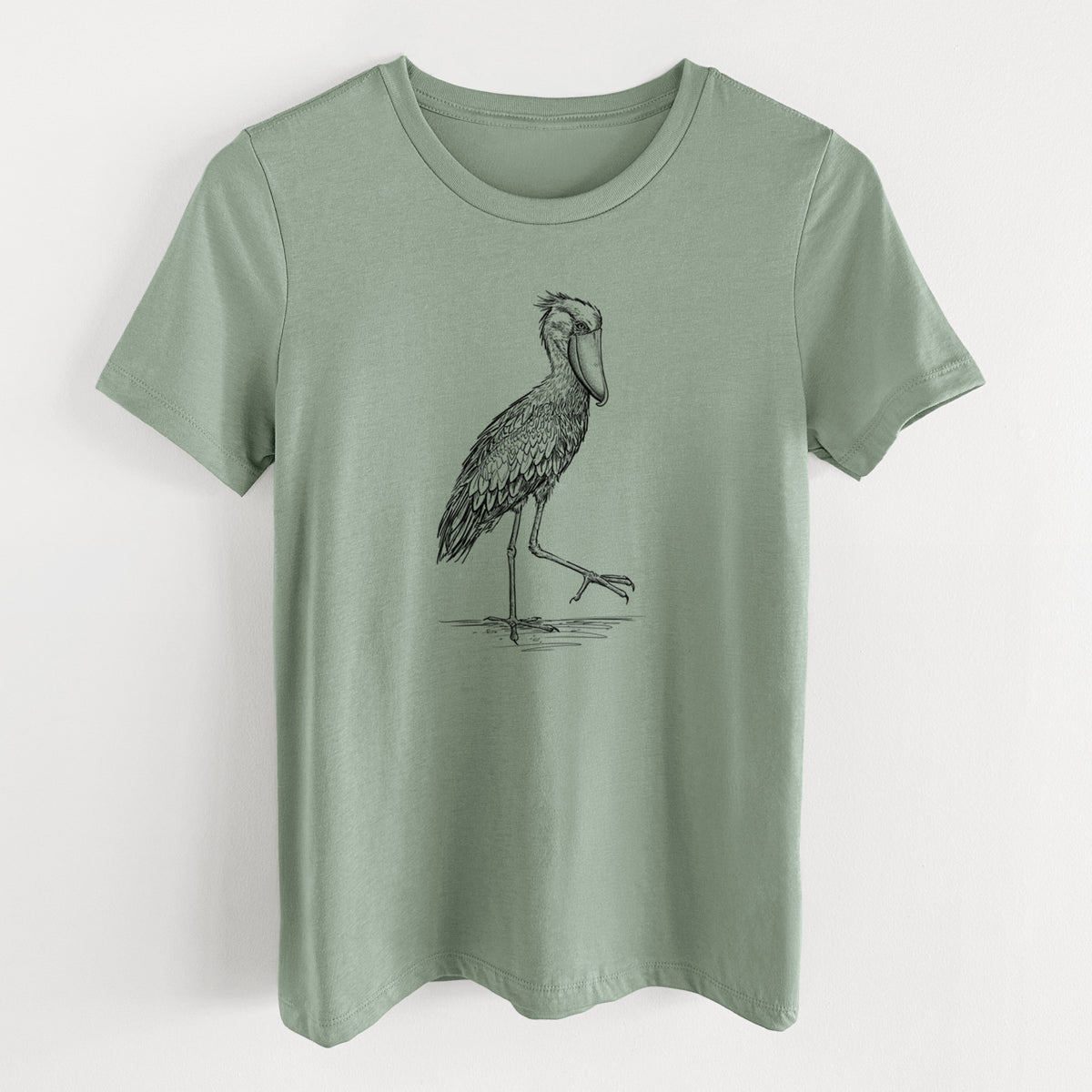 Sage green women's relaxed fit cotton t-shirt laid flat, printed with a black ink illustration of a shoebill stork standing on one leg.