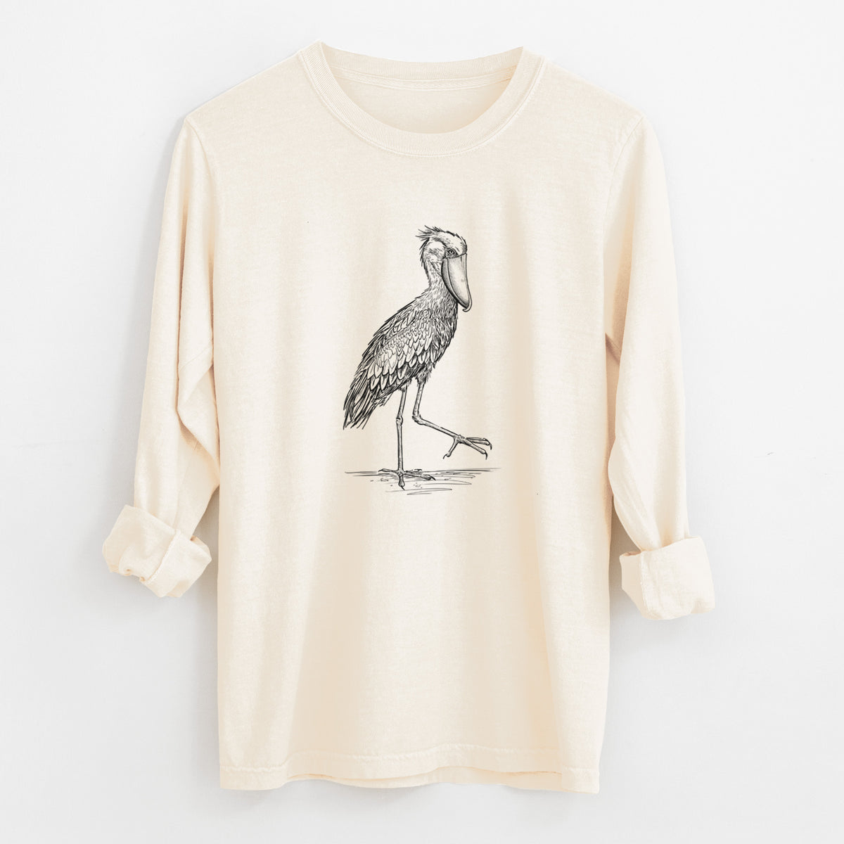 Ivory Comfort Colors long sleeve shirt laid flat with the cuffs rolled, printed with a black ink illustration of a shoebill stork standing on one leg.