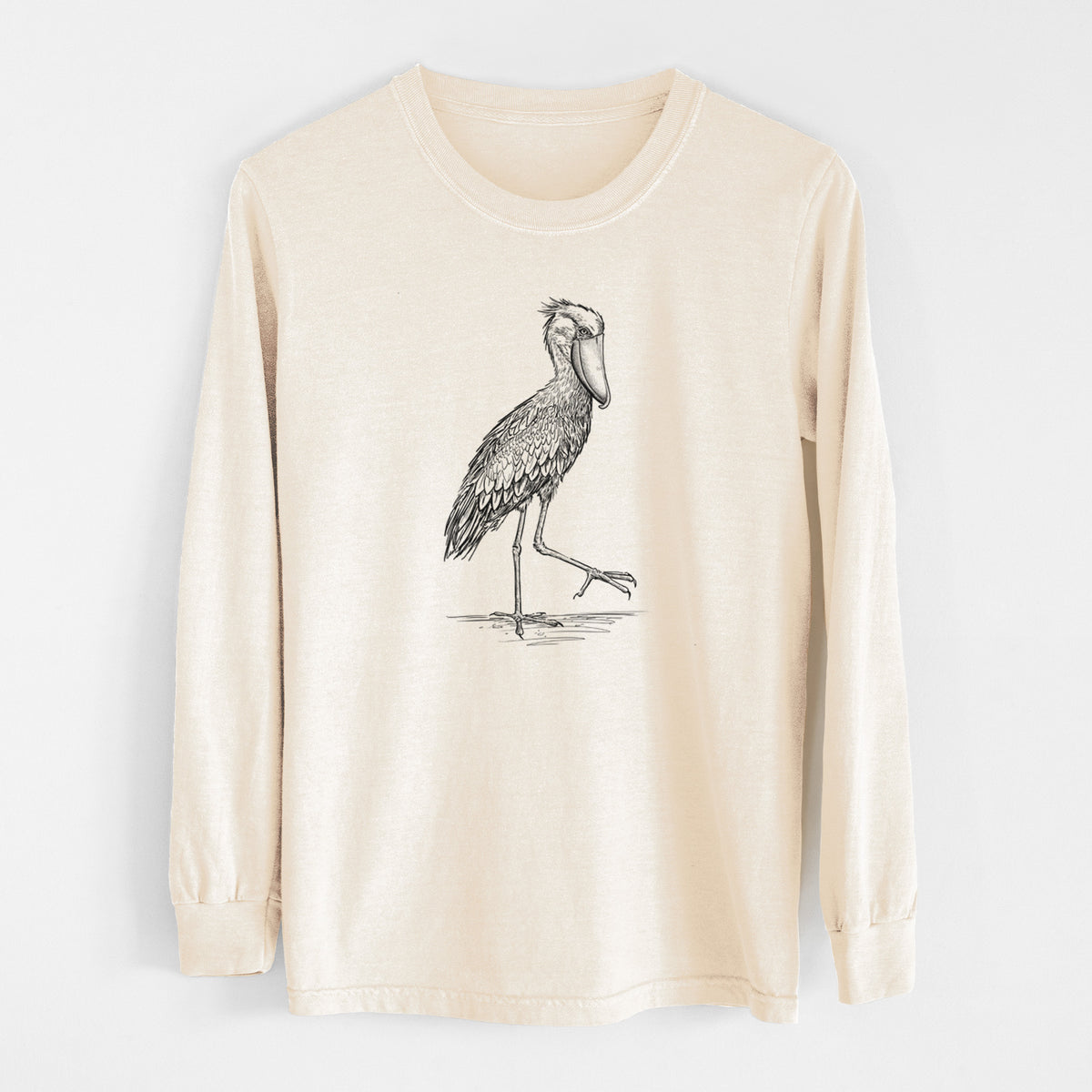 Ivory Comfort Colors long sleeve shirt laid flat, printed with a black ink illustration of a shoebill stork standing on one leg.