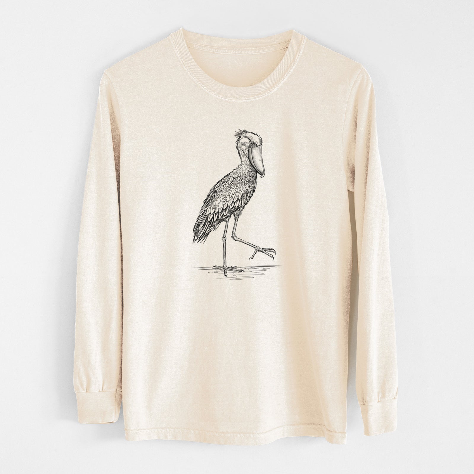 Ivory Comfort Colors long sleeve shirt laid flat, printed with a black ink illustration of a shoebill stork standing on one leg.