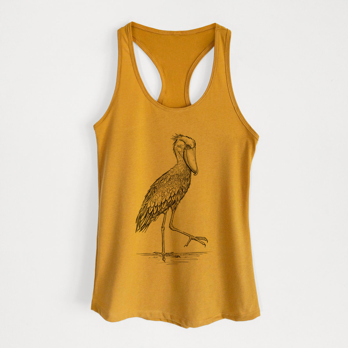 Gold women's racerback tank top laid flat, printed with a black ink illustration of a shoebill stork standing on one leg.