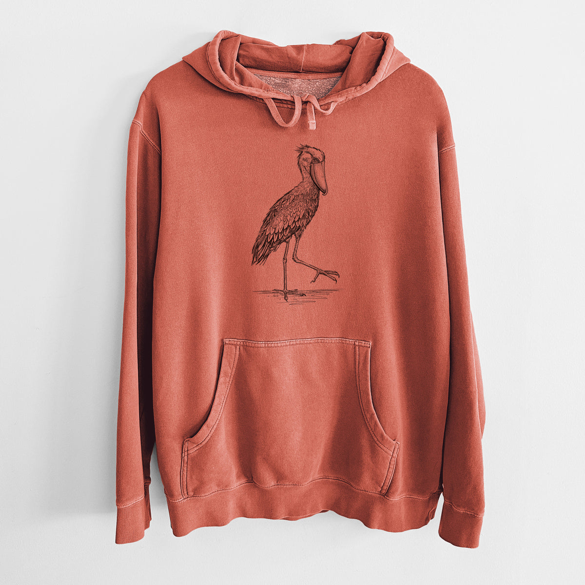 Amber orange pigment dyed hoodie laid flat, printed with a black ink illustration of a shoebill stork standing on one leg.