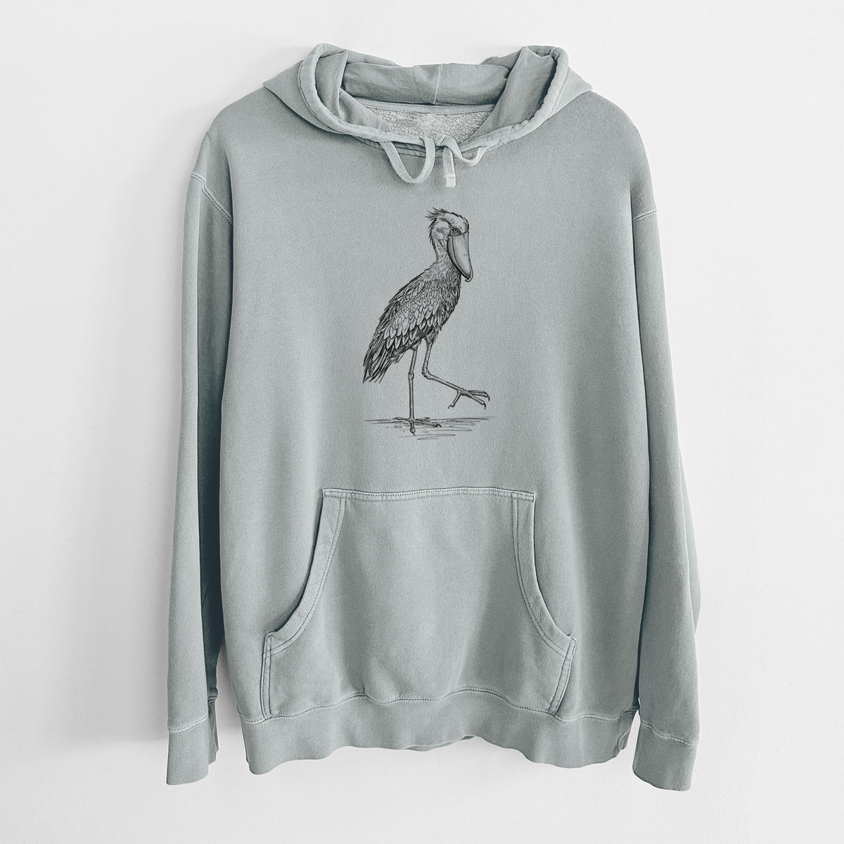 Sage green pigment dyed hoodie laid flat, printed with a black ink illustration of a shoebill stork standing on one leg.