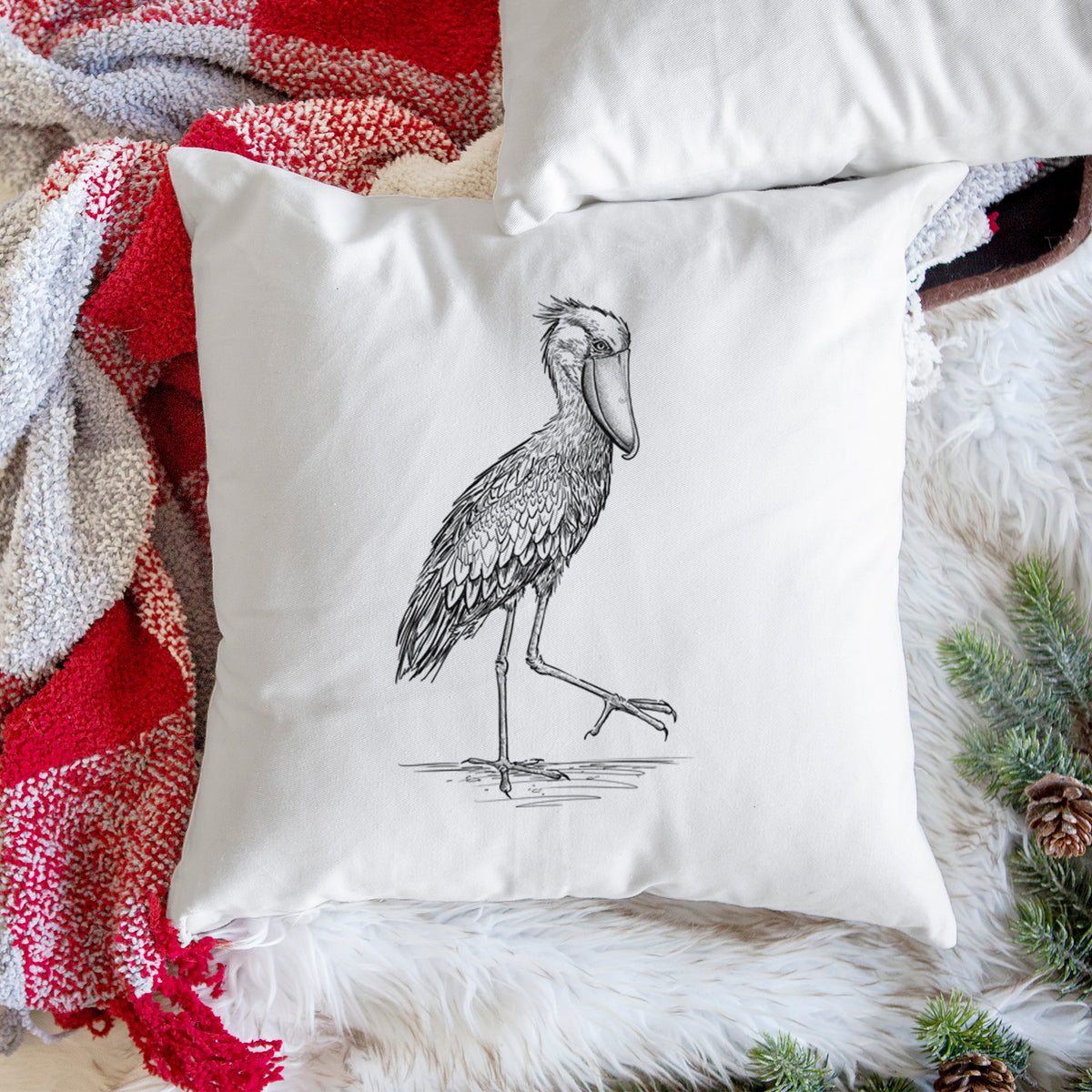 White pillow cover printed with a black ink illustration of a shoebill stork standing on one leg, on a woven chair.