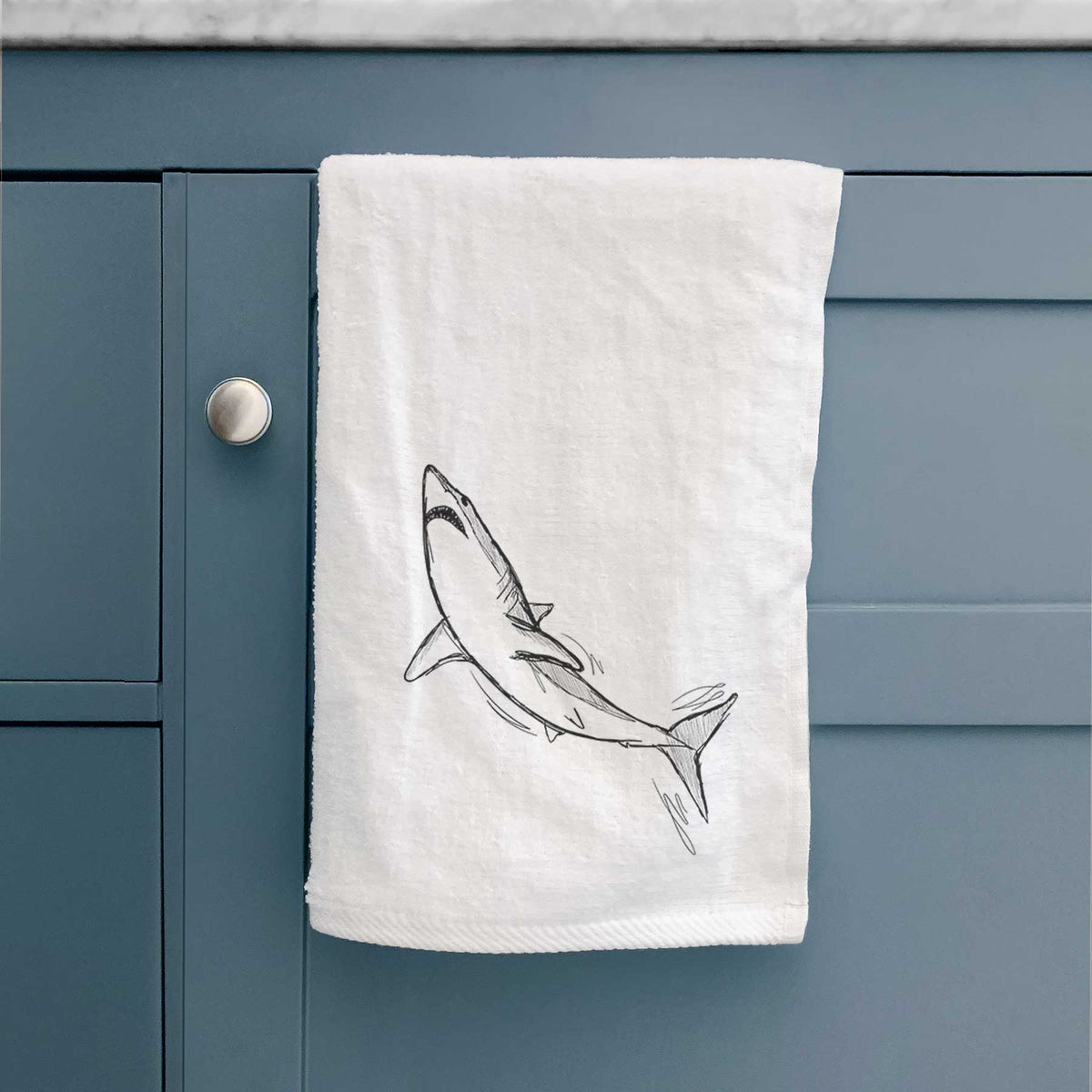 White hand towel printed with a black ink illustration of a shortfin mako shark diving, hanging on a cabinet door.