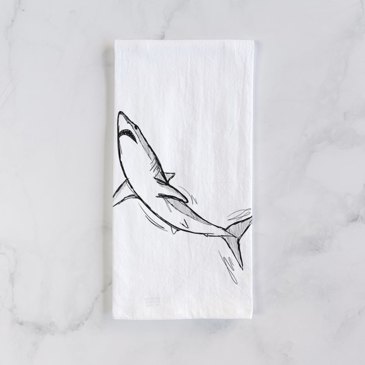White cotton tea towel laid flat on marble, printed with a black ink illustration of a shortfin mako shark diving.