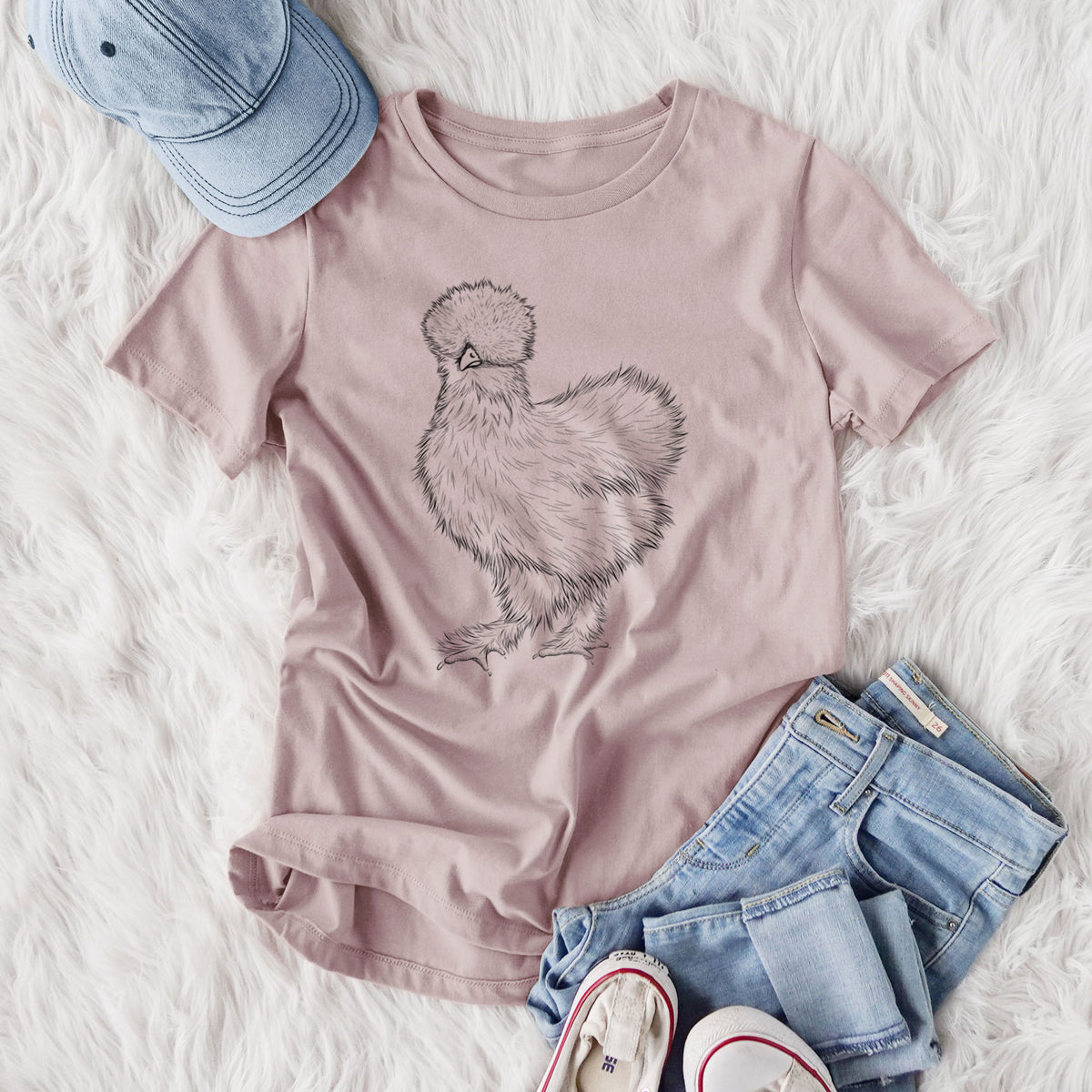 Women's relaxed fit cotton t-shirt printed with a black ink illustration of a fluffy silkie chicken, styled flat on a white faux fur rug with jeans.