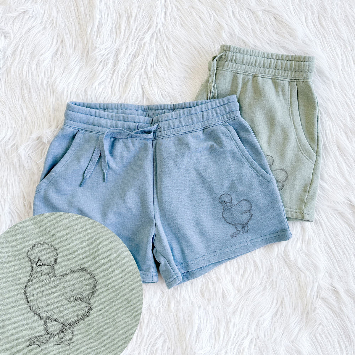 Two pairs of Cali Wave shorts in different colors printed with a black ink illustration of a fluffy silkie chicken, with a close-up of the print.