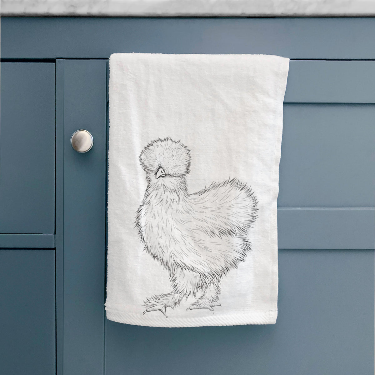 White hand towel printed with a black ink illustration of a fluffy silkie chicken, hanging on a cabinet door.