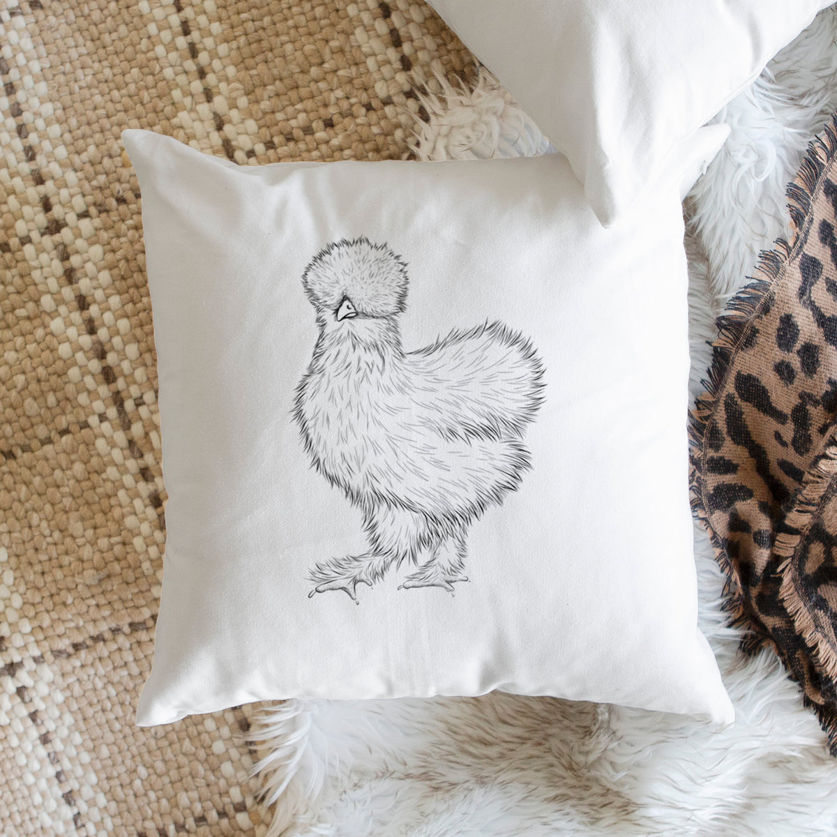 White pillow cover printed with a black ink illustration of a fluffy silkie chicken, on a woven chair.