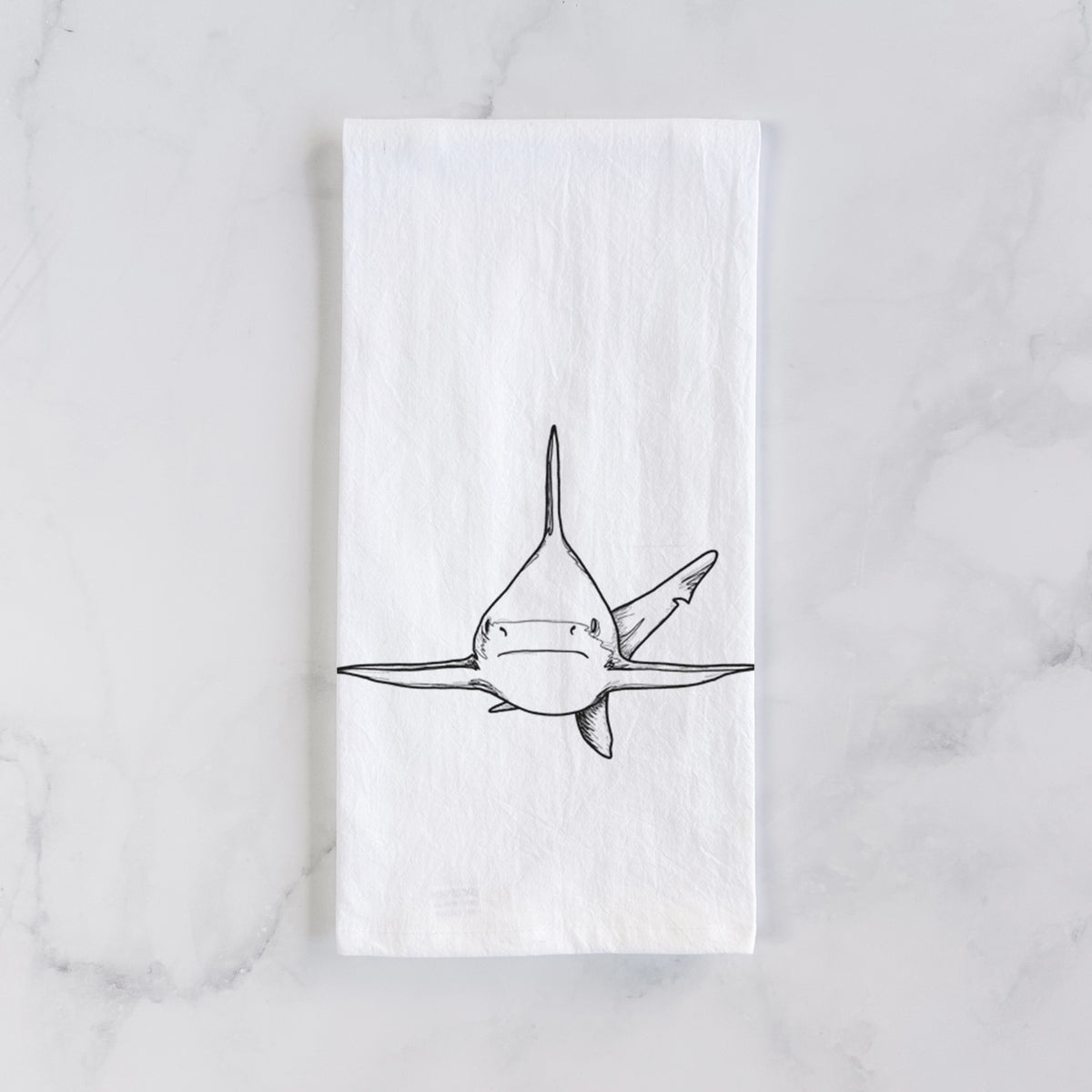 White cotton tea towel laid flat on marble, printed with a black ink illustration of a silvertip shark swimming head-on.