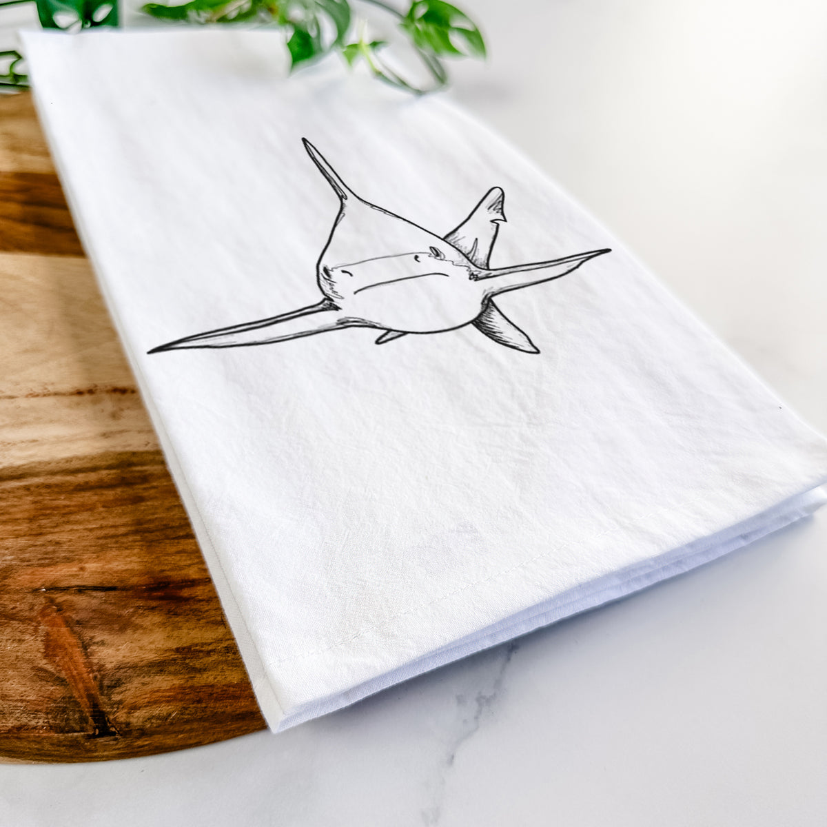 Close-up of a folded white tea towel on a wooden board, showing a black ink illustration of a silvertip shark swimming head-on.