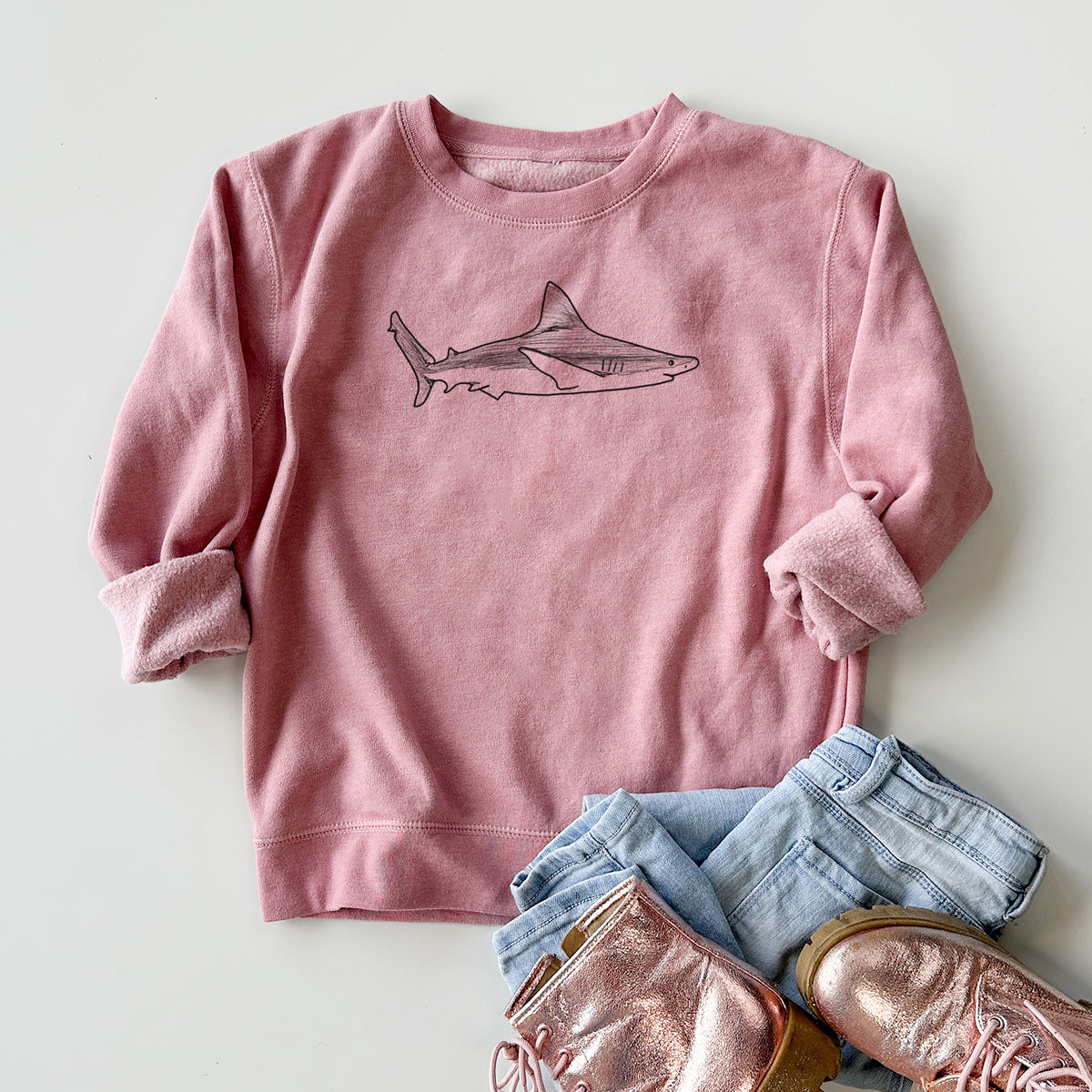 Youth crewneck sweatshirt printed with a black ink illustration of a silvertip shark swimming in profile, styled flat with jeans and boots.