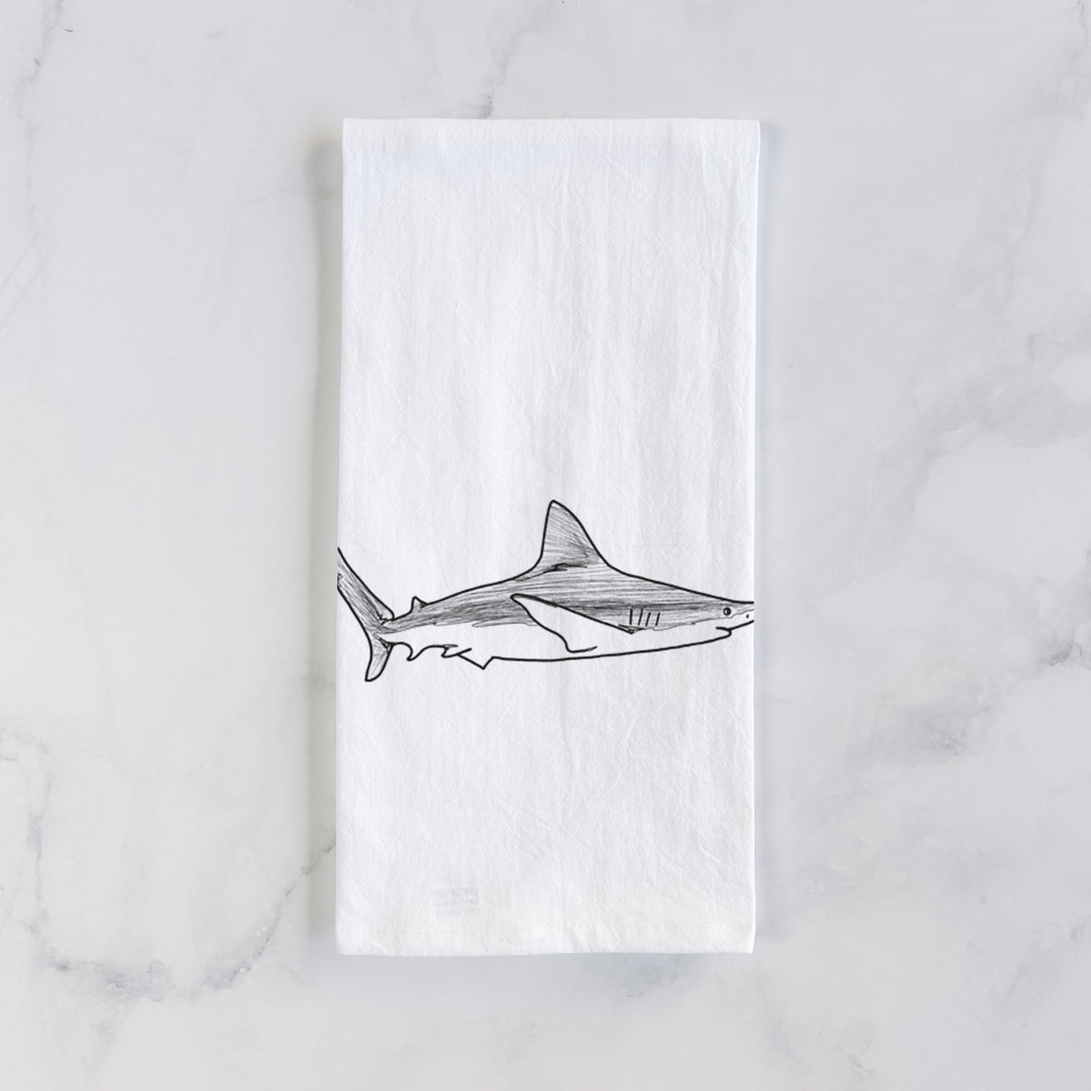 White cotton tea towel laid flat on marble, printed with a black ink illustration of a silvertip shark swimming in profile.
