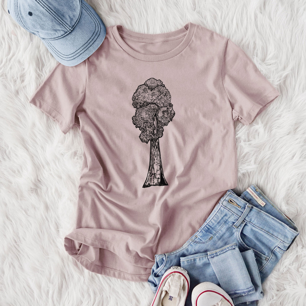 Women's relaxed fit cotton t-shirt printed with a black ink illustration of a single giant sequoia tree, styled flat on a white faux fur rug with jeans.