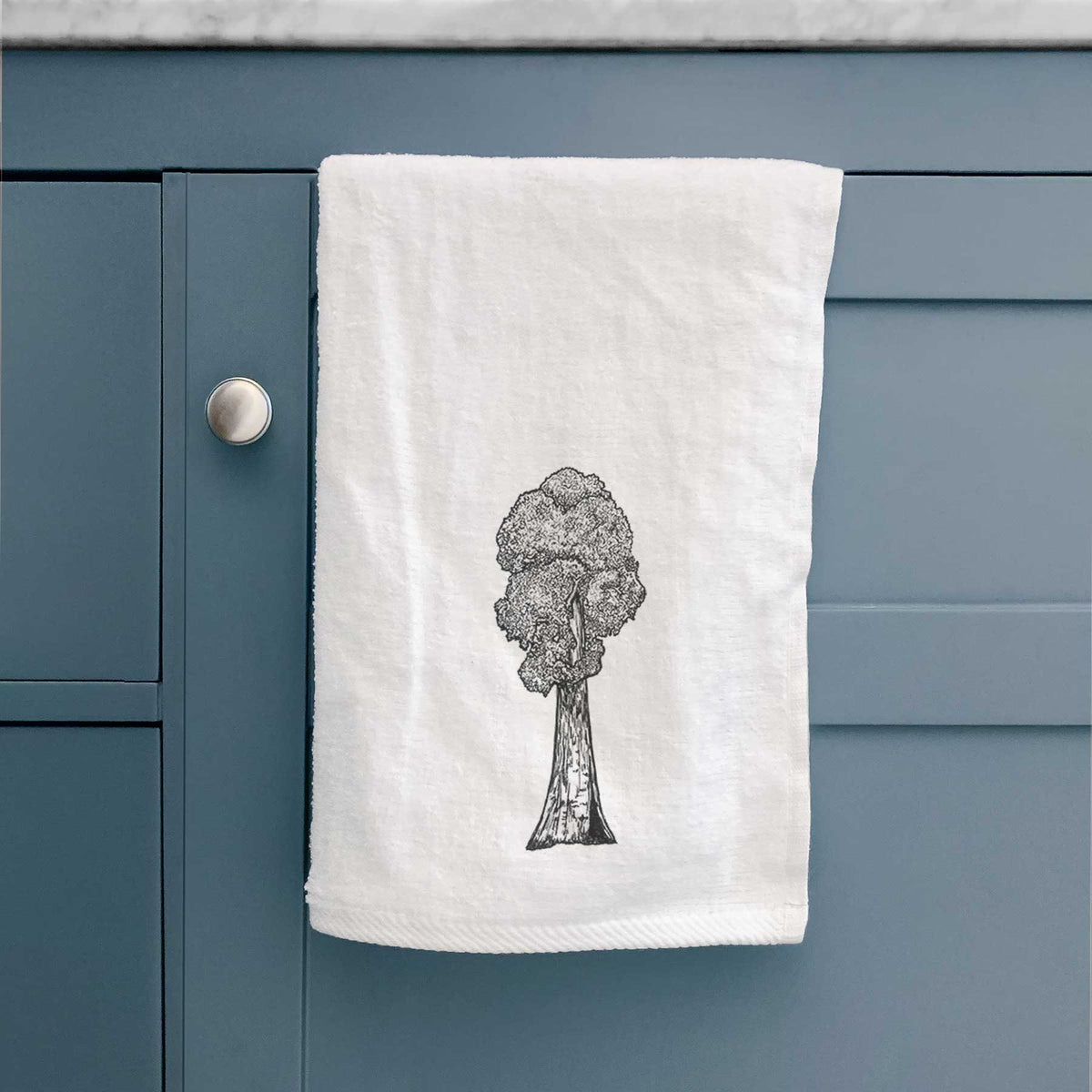 White hand towel printed with a black ink illustration of a single giant sequoia tree, hanging on a cabinet door.