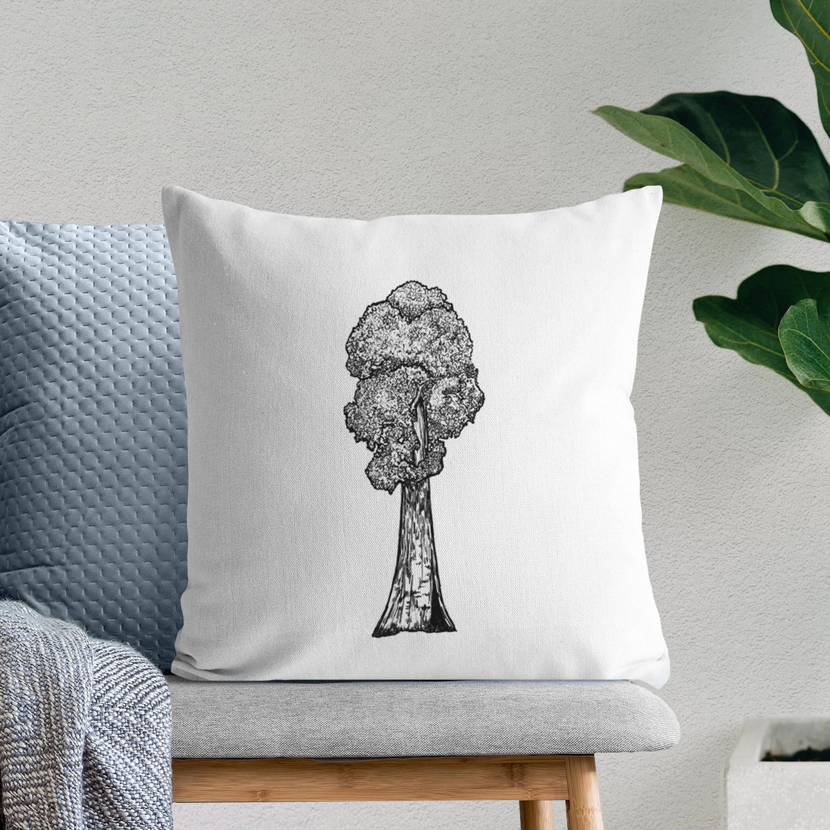 White pillow cover printed with a black ink illustration of a single giant sequoia tree, on a bench beside plants.