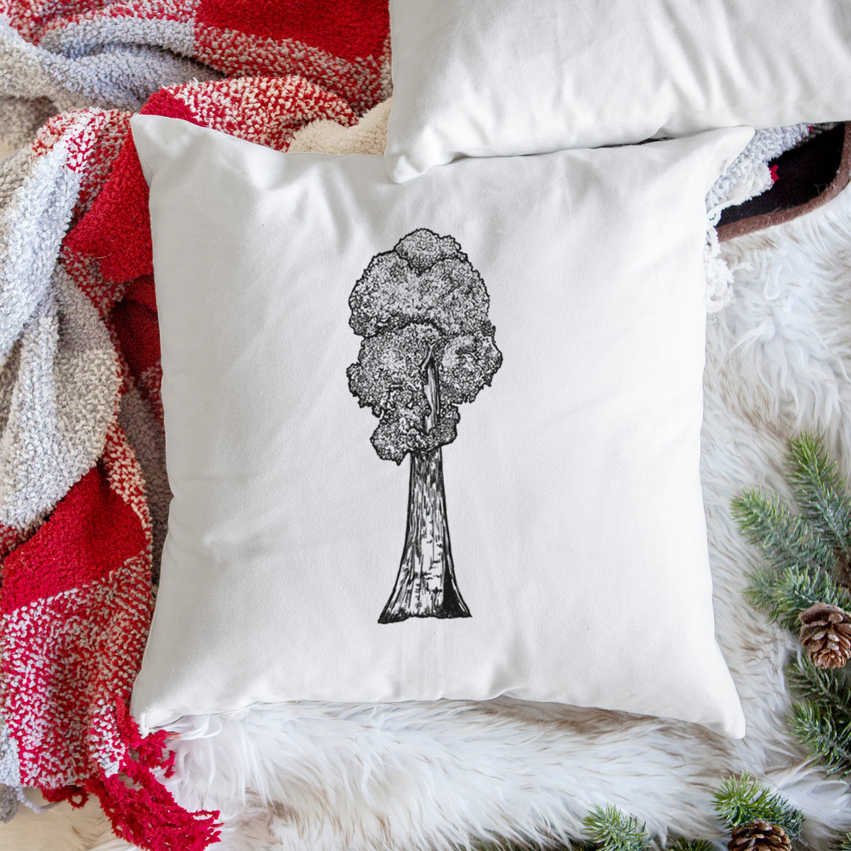 White pillow cover printed with a black ink illustration of a single giant sequoia tree, on a woven chair.