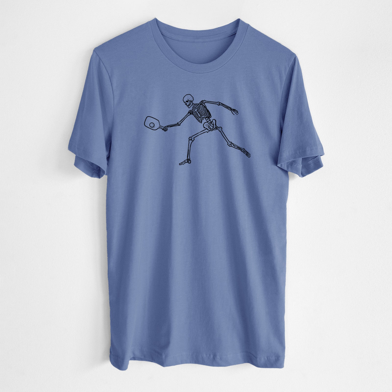 Blue bell lightweight cotton t-shirt laid flat, printed with a black ink skeleton lunging to hit a pickleball with a paddle.