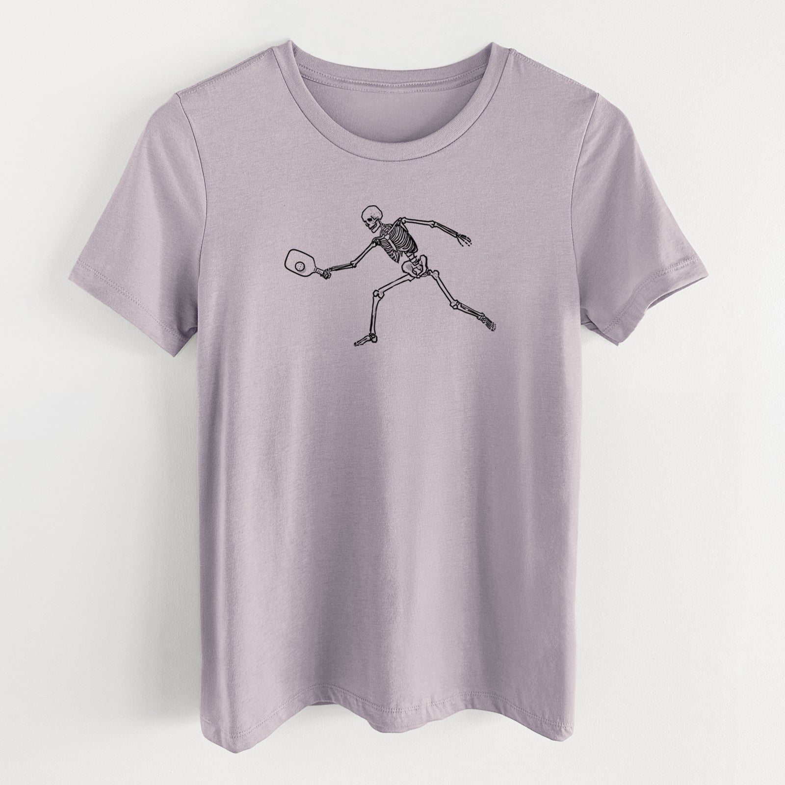 Light violet women's relaxed fit cotton t-shirt laid flat, printed with a black ink skeleton lunging to hit a pickleball with a paddle.