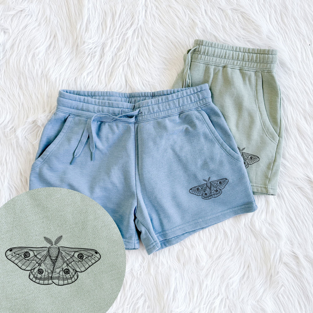 Two pairs of Cali Wave shorts in different colors printed with a detailed black ink illustration of a small emperor moth with eyespots on its wings, with a close-up of the print.