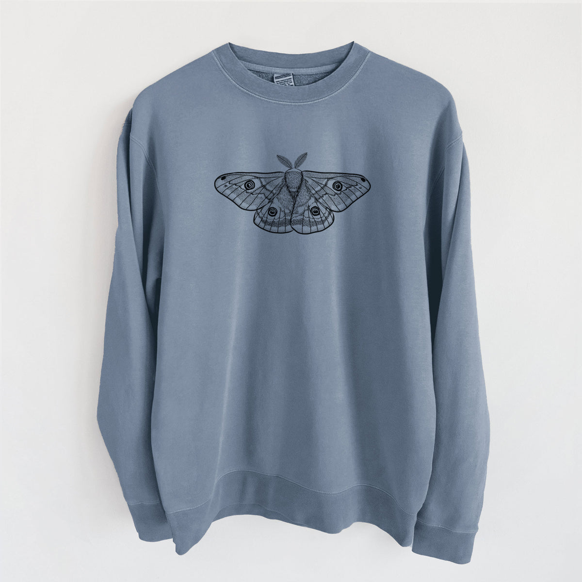 Slate blue pigment dyed crewneck sweatshirt laid flat, printed with a detailed black ink illustration of a small emperor moth with eyespots on its wings.