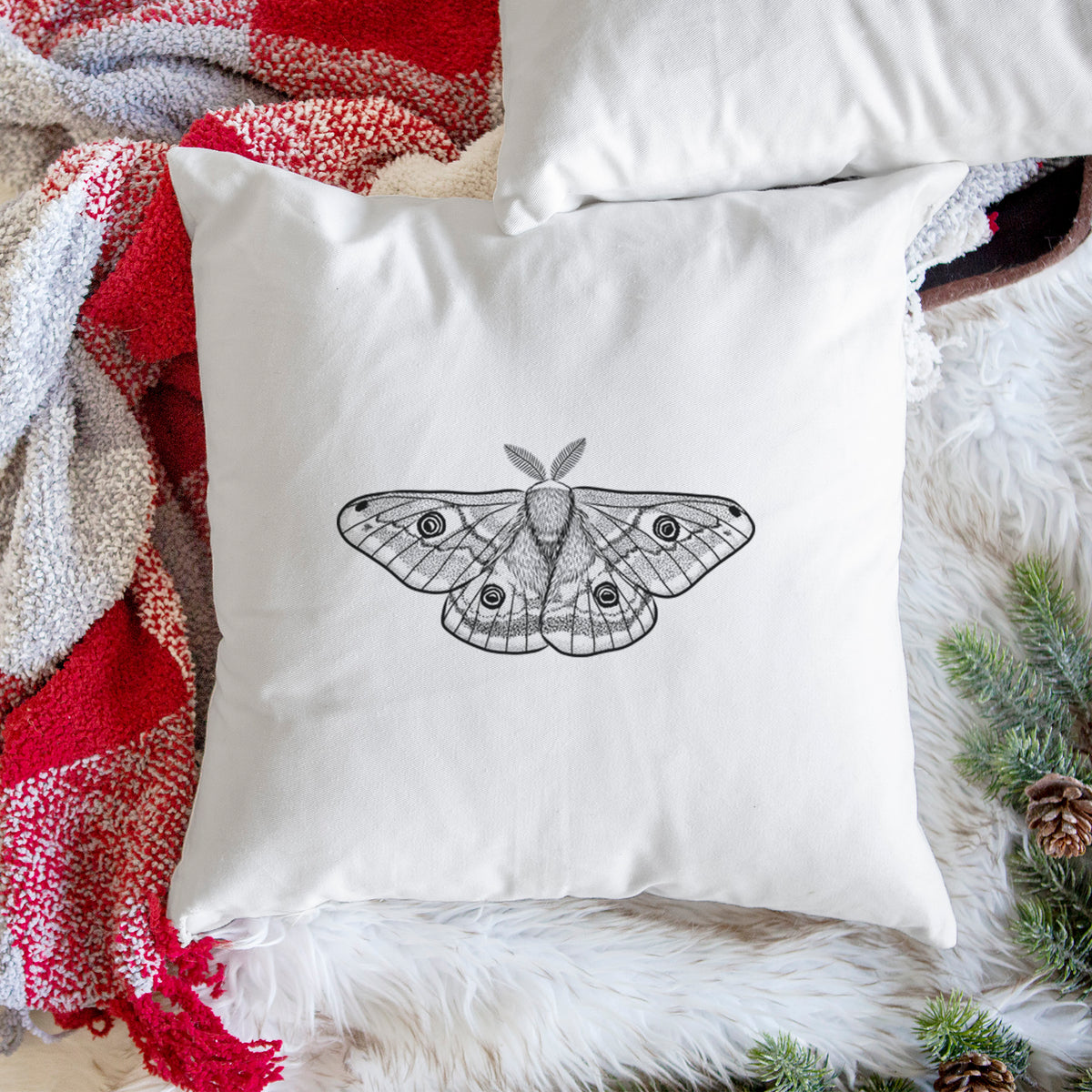White pillow cover printed with a detailed black ink illustration of a small emperor moth with eyespots on its wings, on a woven chair.