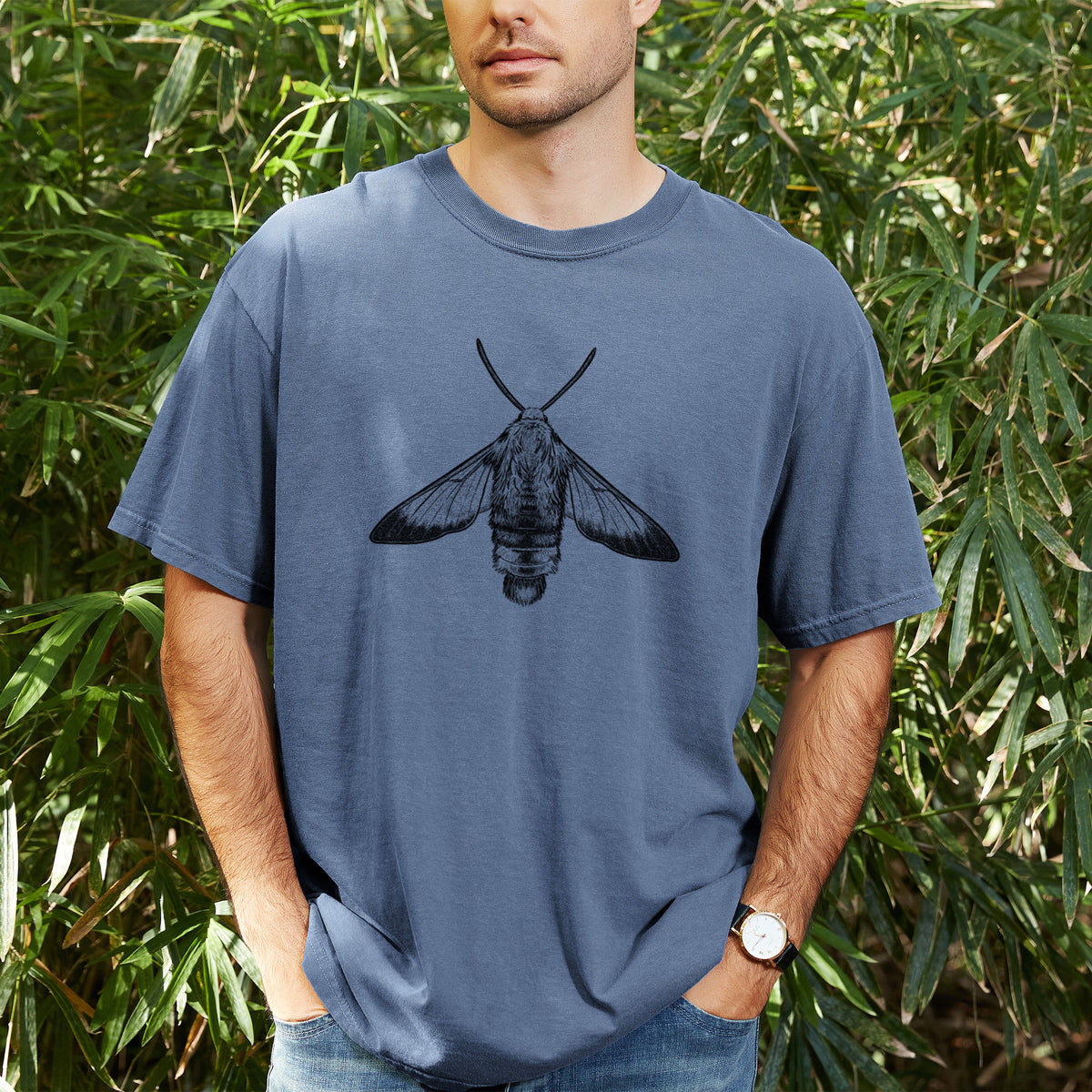 Man wearing a Comfort Colors t-shirt printed with a detailed black ink illustration of a snowberry clearwing moth, seen from above, outdoors.