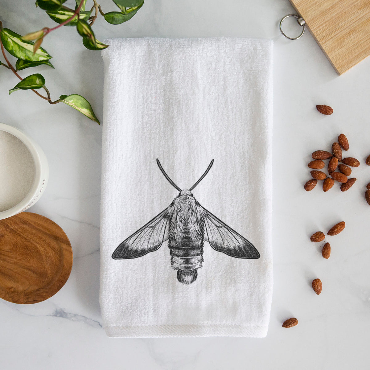 White hand towel printed with a detailed black ink illustration of a snowberry clearwing moth, seen from above.