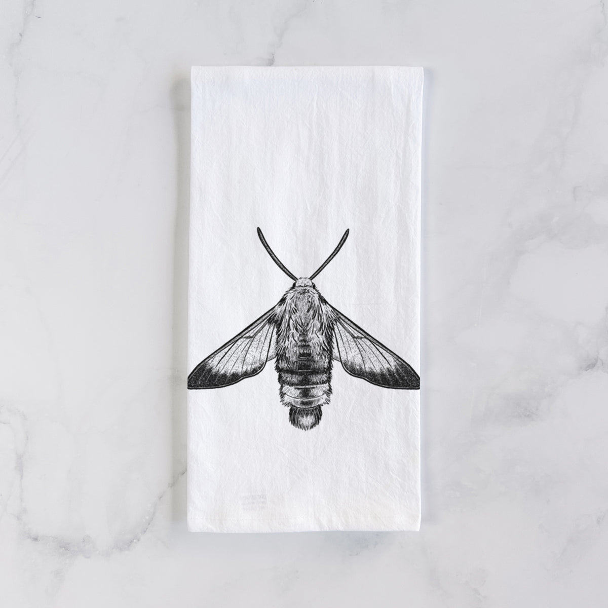 White cotton tea towel laid flat on marble, printed with a detailed black ink illustration of a snowberry clearwing moth, seen from above.