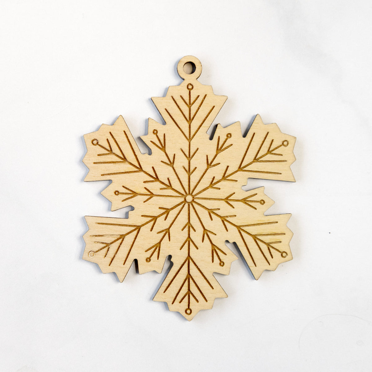 Wooden ornament featuring an engraved geometric snowflake design, on a marble surface.
