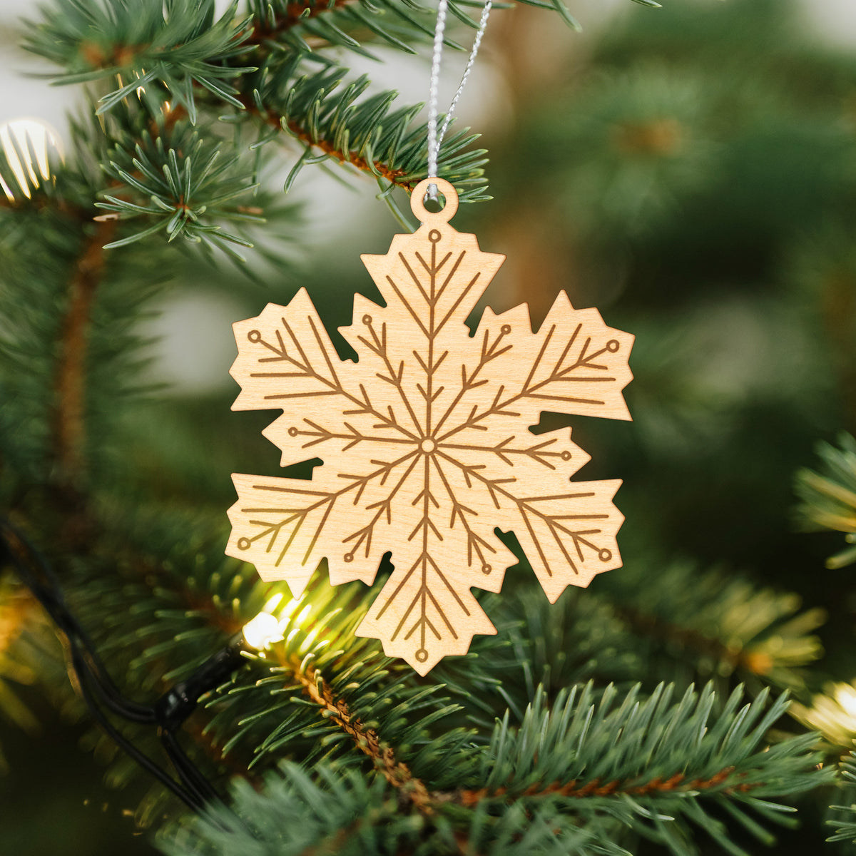 Wooden ornament featuring an engraved geometric snowflake design, hanging on a Christmas tree.