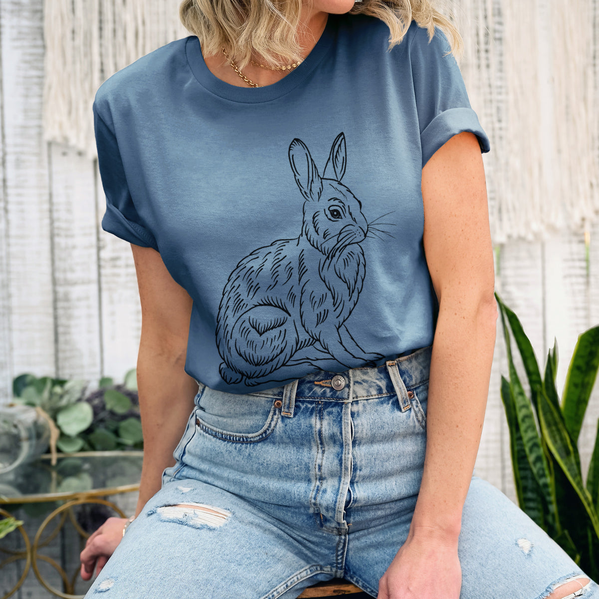 Woman wearing a steel blue lightweight cotton t-shirt printed with a detailed black ink illustration of a snowshoe hare sitting upright.