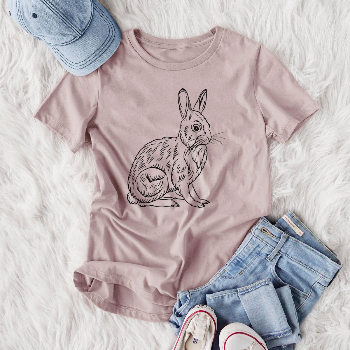 Women's relaxed fit cotton t-shirt printed with a detailed black ink illustration of a snowshoe hare sitting upright, styled flat on a white faux fur rug with jeans.