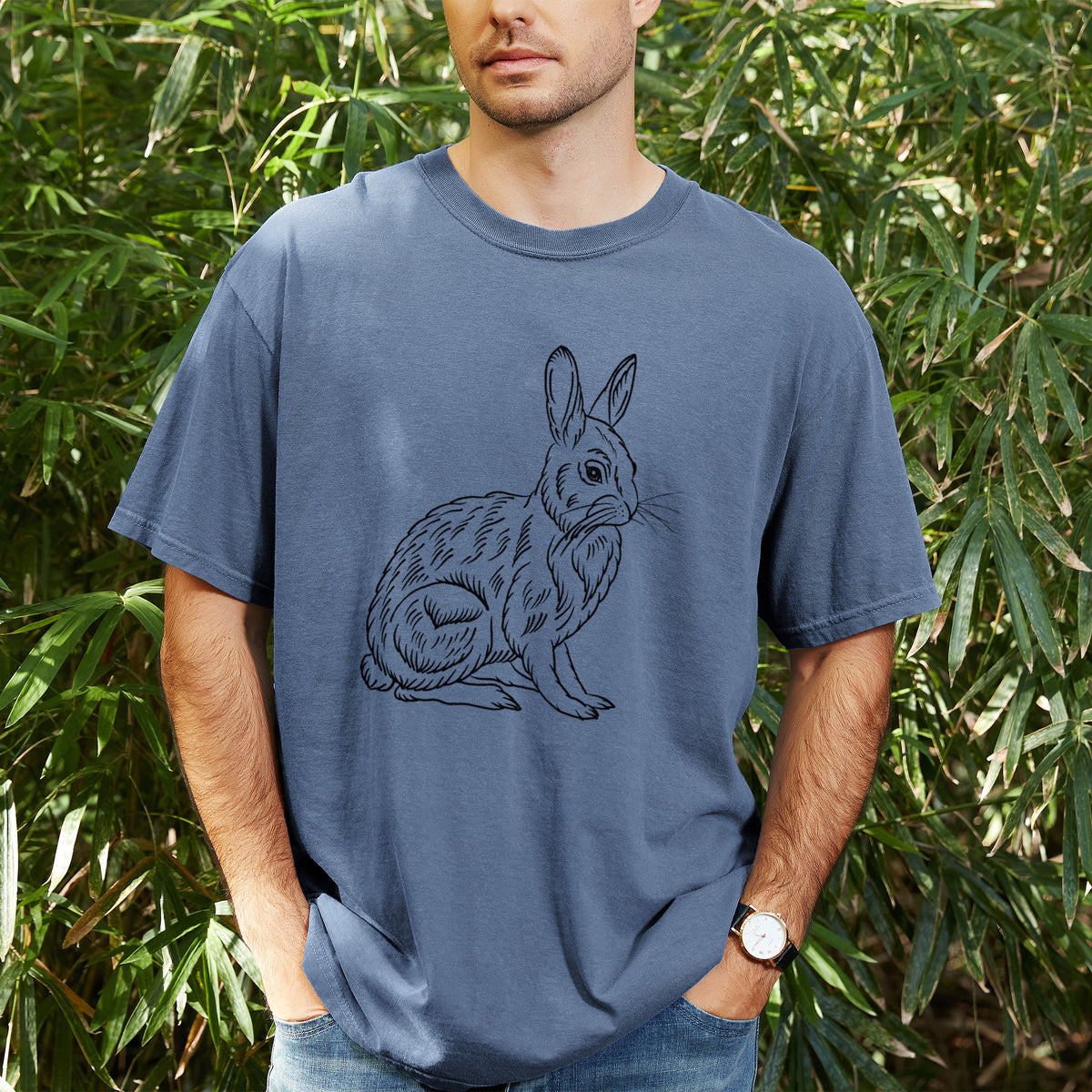 Man wearing a Comfort Colors t-shirt printed with a detailed black ink illustration of a snowshoe hare sitting upright, outdoors.