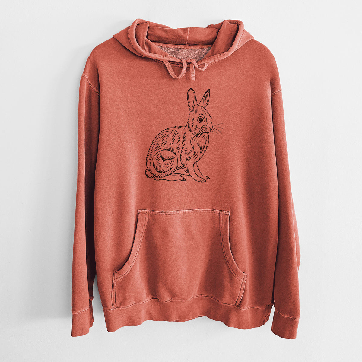 Amber orange pigment dyed hoodie laid flat, printed with a detailed black ink illustration of a snowshoe hare sitting upright.