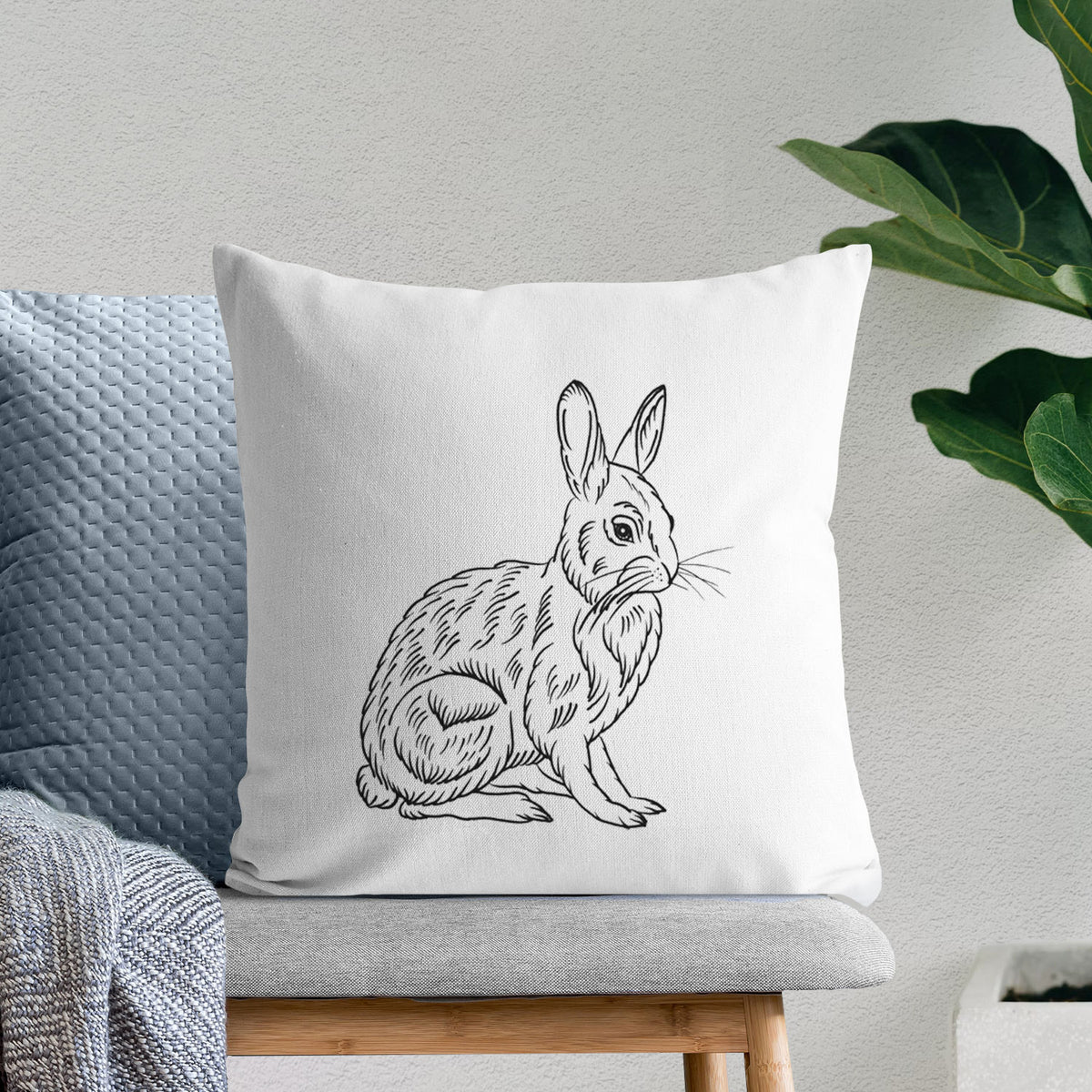 White pillow cover printed with a detailed black ink illustration of a snowshoe hare sitting upright, on a bench beside plants.