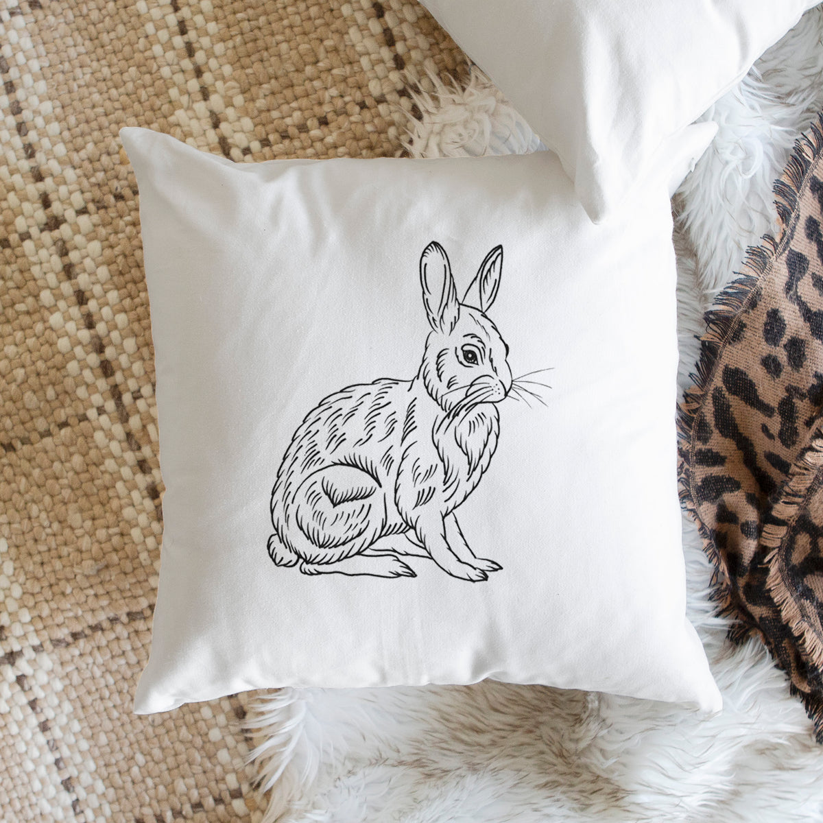 White pillow cover printed with a detailed black ink illustration of a snowshoe hare sitting upright, on a woven chair.