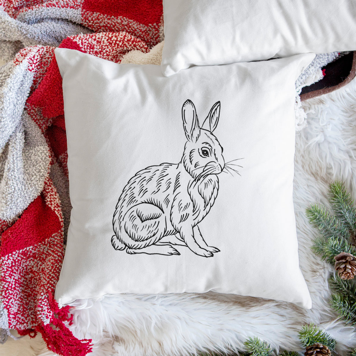 White pillow cover printed with a detailed black ink illustration of a snowshoe hare sitting upright, on a woven chair.