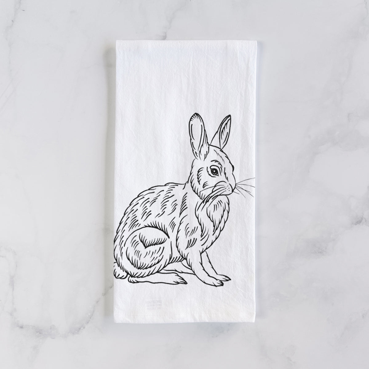 White cotton tea towel laid flat on marble, printed with a detailed black ink illustration of a snowshoe hare sitting upright.