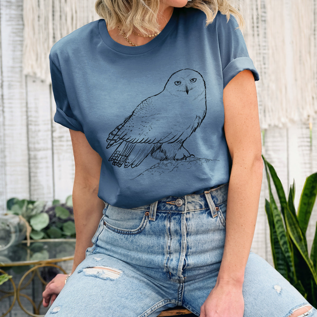 Woman wearing a steel blue lightweight cotton t-shirt printed with a detailed black ink illustration of a snowy owl perched on a snowy mound.
