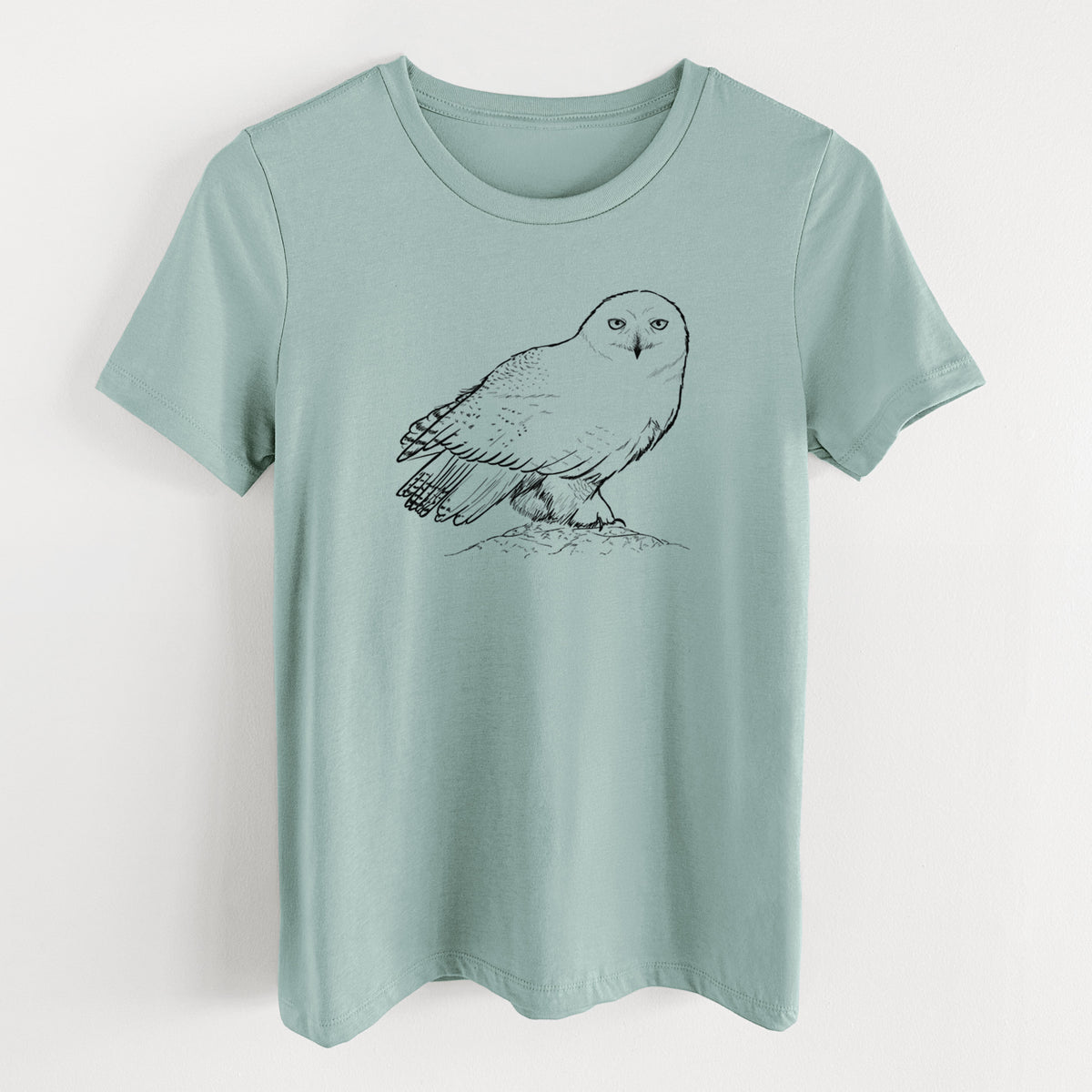 Dusty blue women's relaxed fit cotton t-shirt laid flat, printed with a detailed black ink illustration of a snowy owl perched on a snowy mound.